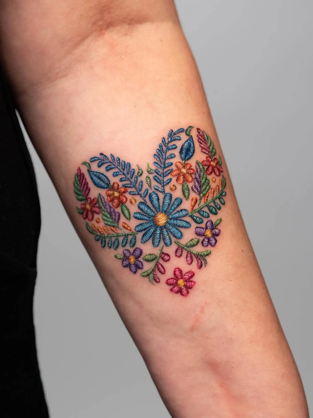 Colorful floral embroidery tattoo on forearm