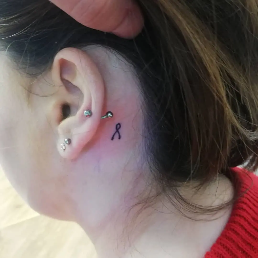 A subtle black ribbon tattoo behind the ear