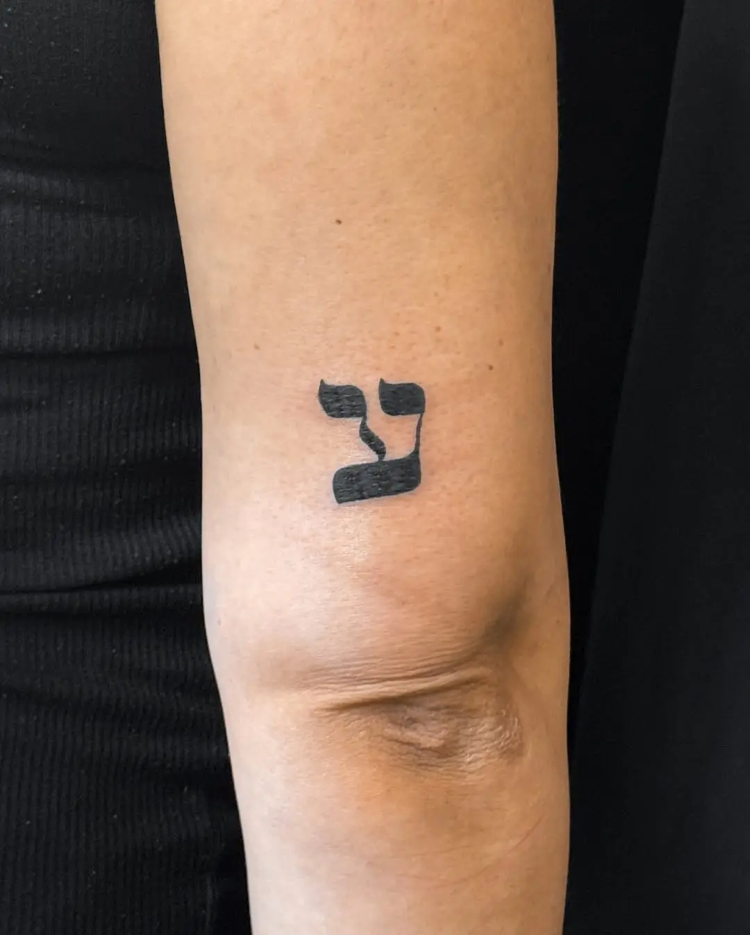 Minimalist Hebrew tattoo on the elbow area