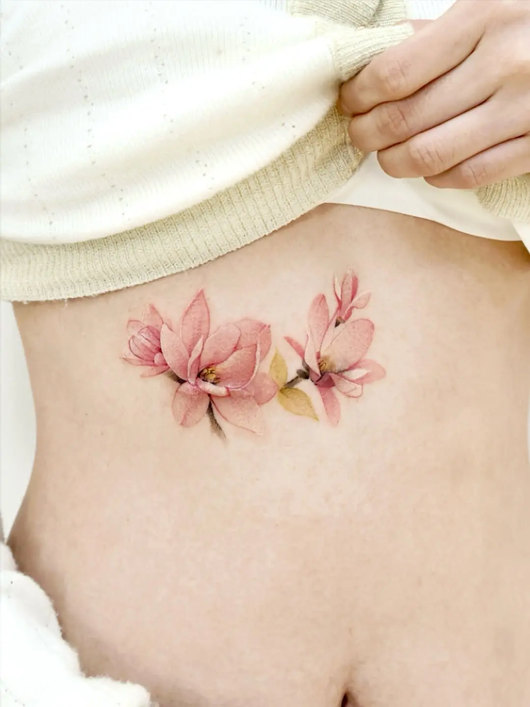 Delicate pink magnolia tattoo on the rib
