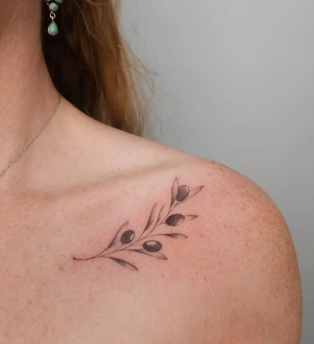 Delicate olive branch tattoo on shoulder area