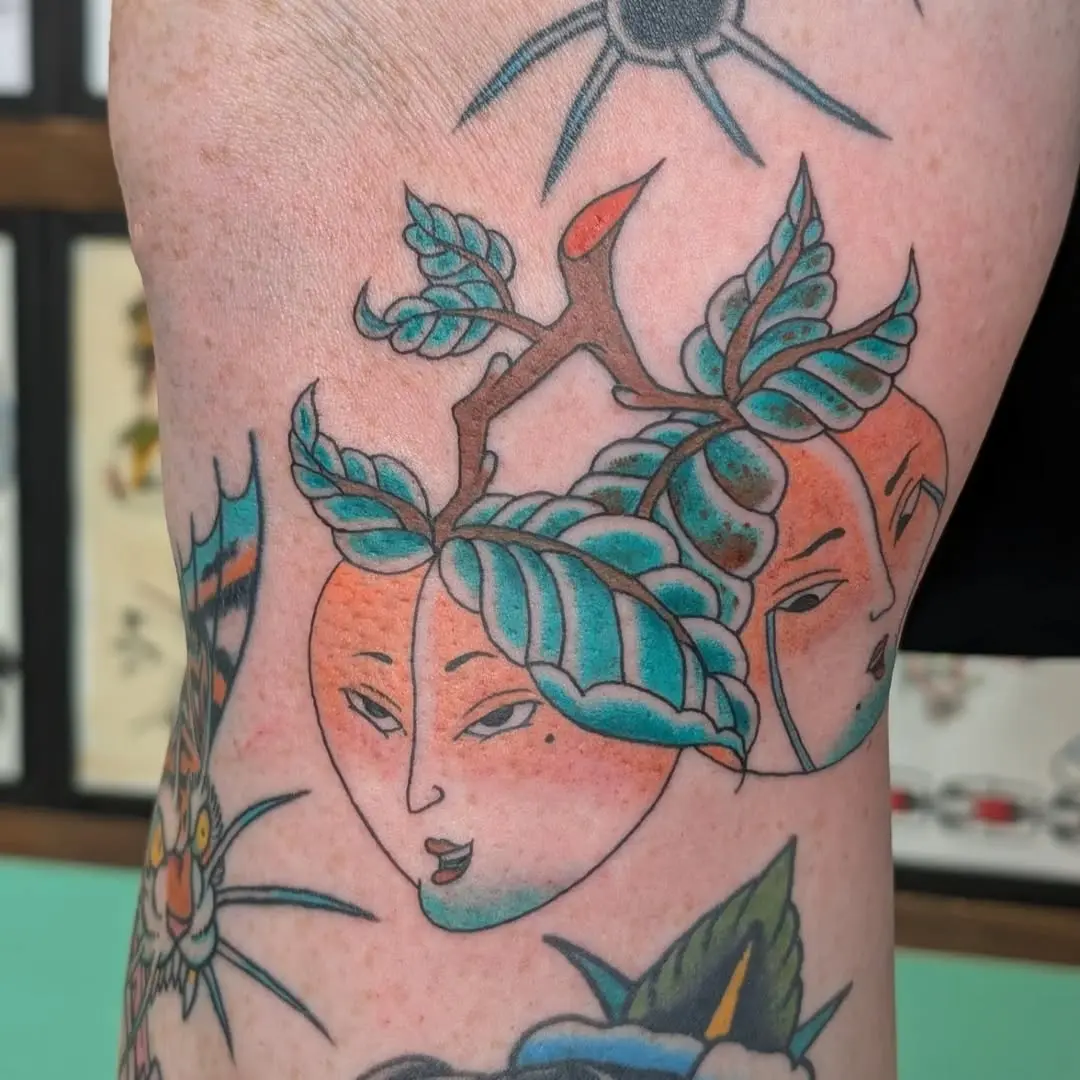Artistic peach tattoo with whimsical faces.