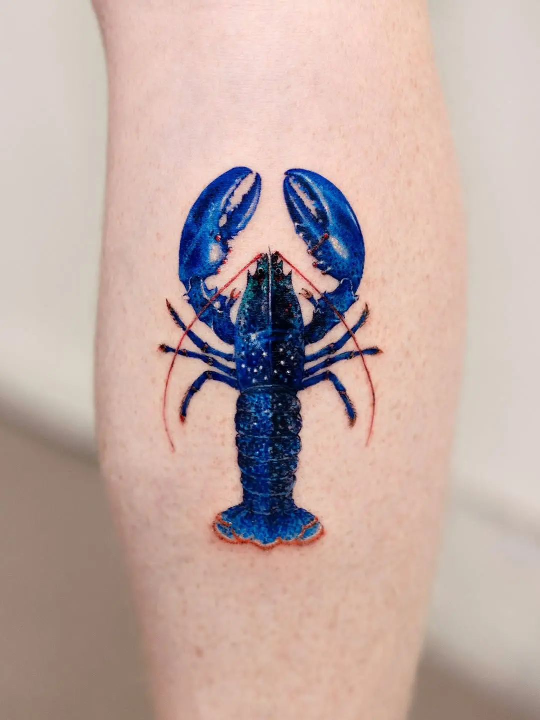 Vibrant blue lobster tattoo on forearm