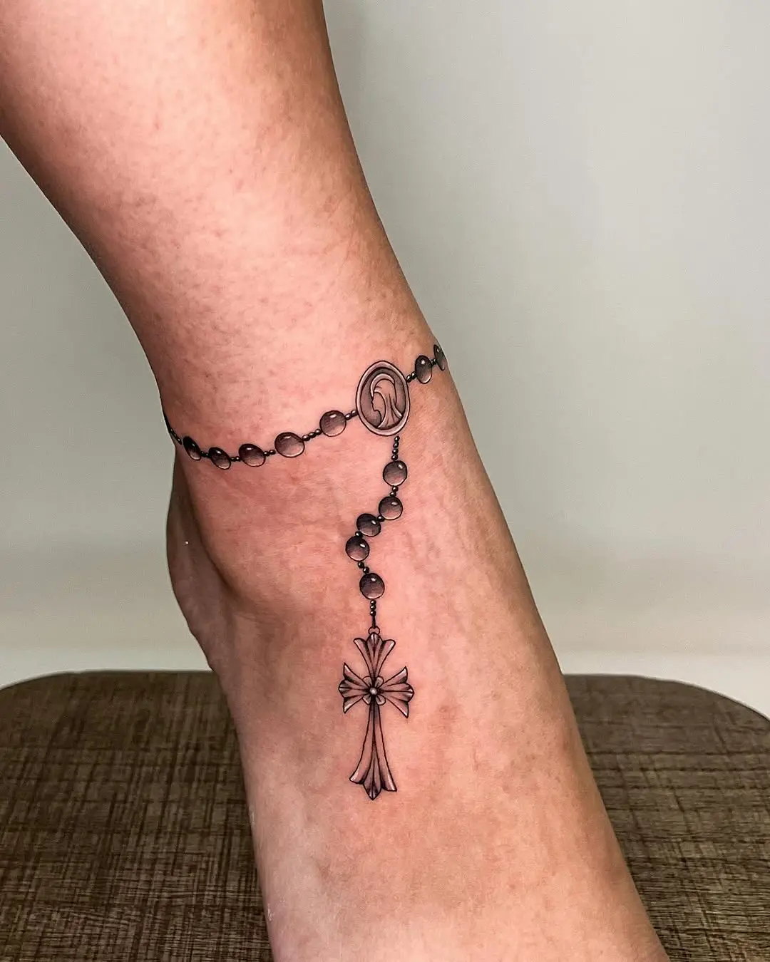 Elegant rosary tattoo adorning the ankle
