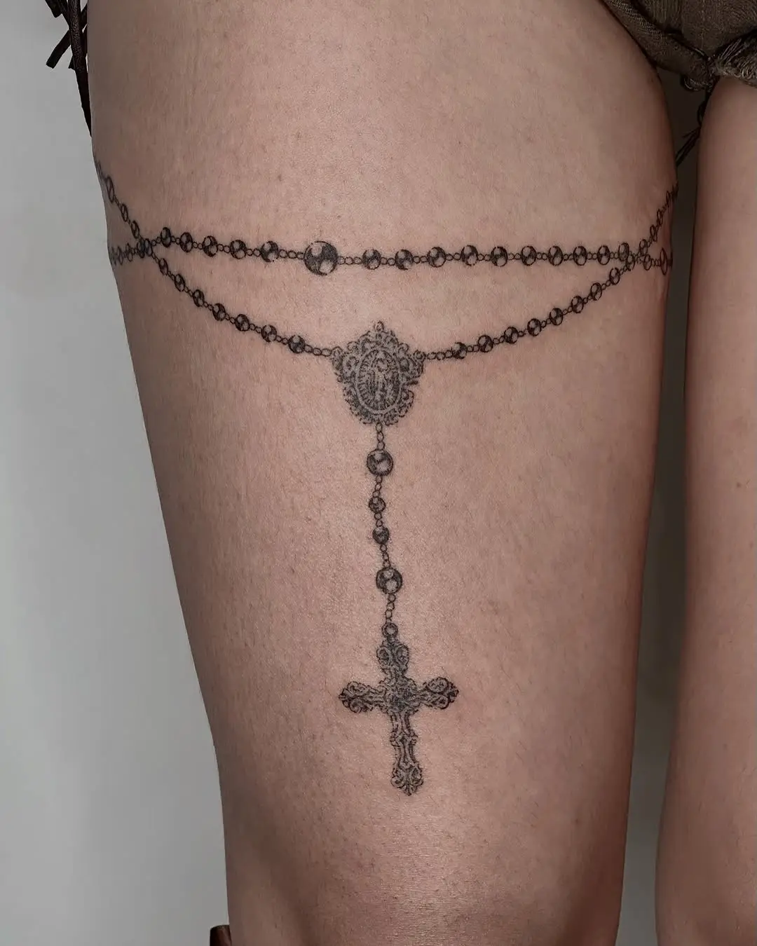 Intricate thigh rosary tattoo with cross element