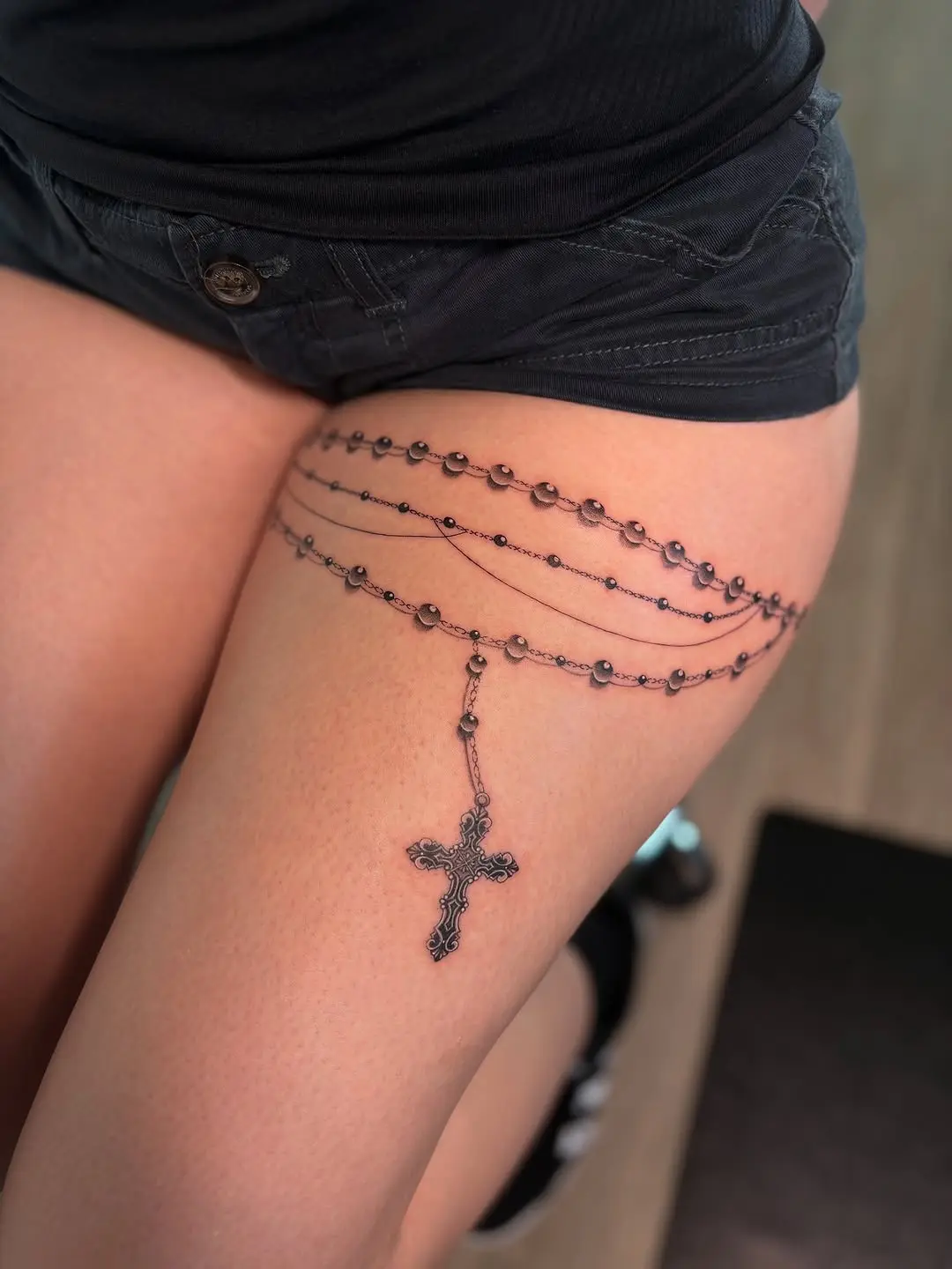 Elegant rosary tattoo draping over the thigh.