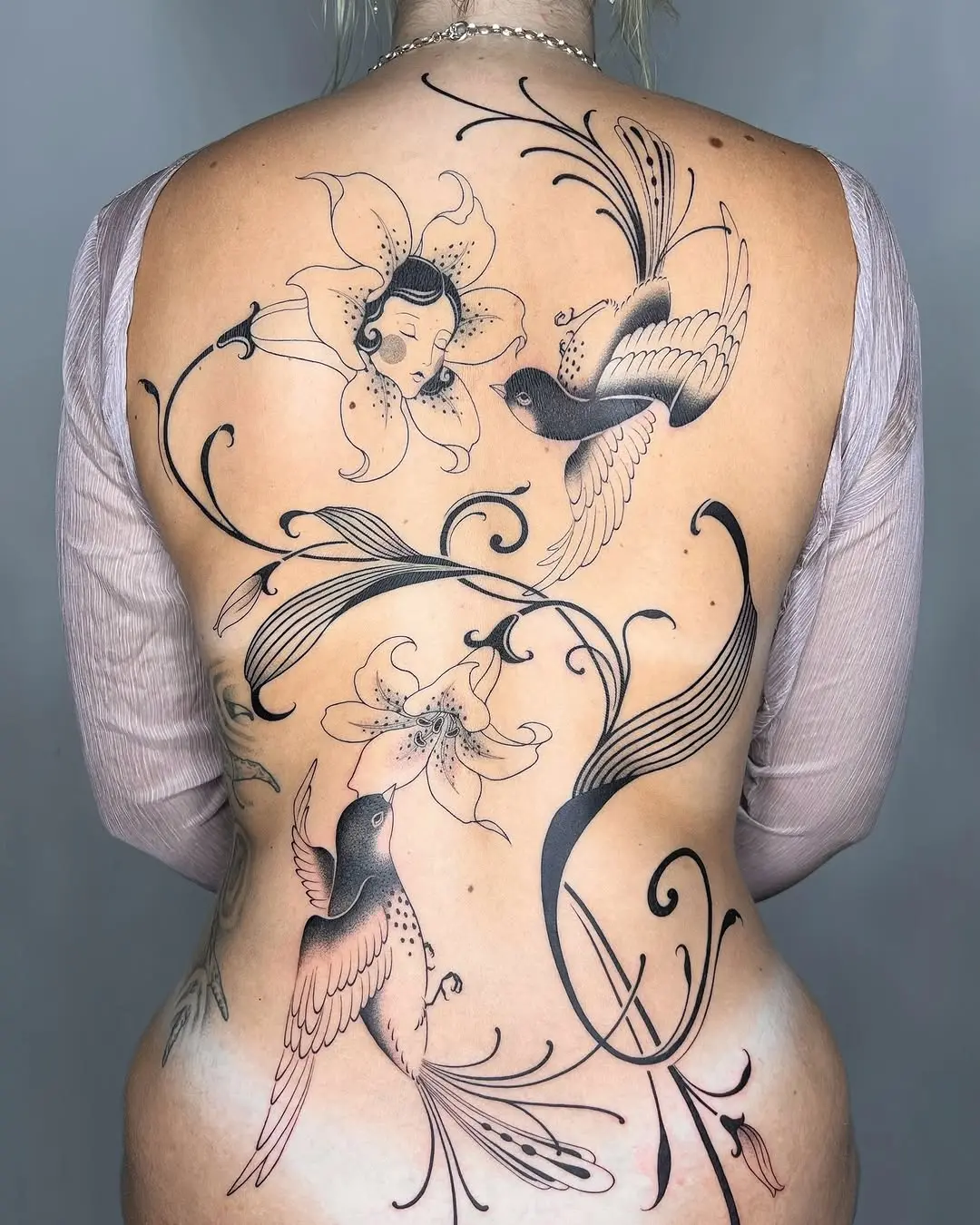 Delicate lilies with elegant birds tattooed beautifully