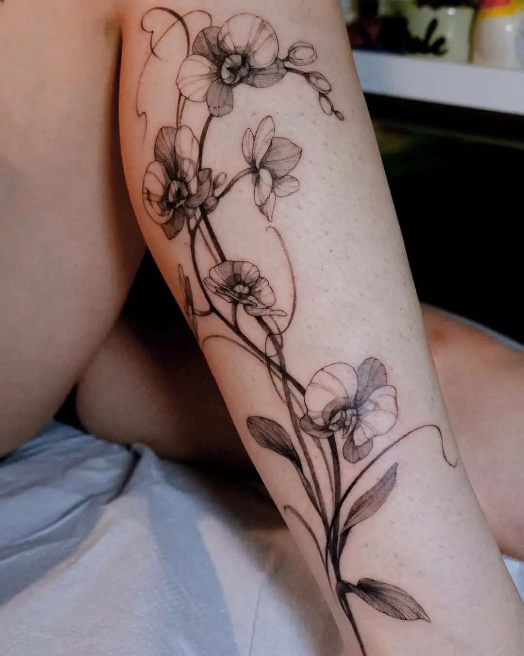 Elegant orchid tattoo wrapping around the leg