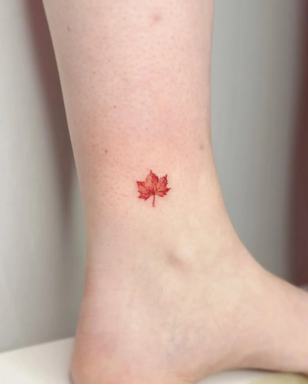 Charming red maple leaf tattoo on the ankle