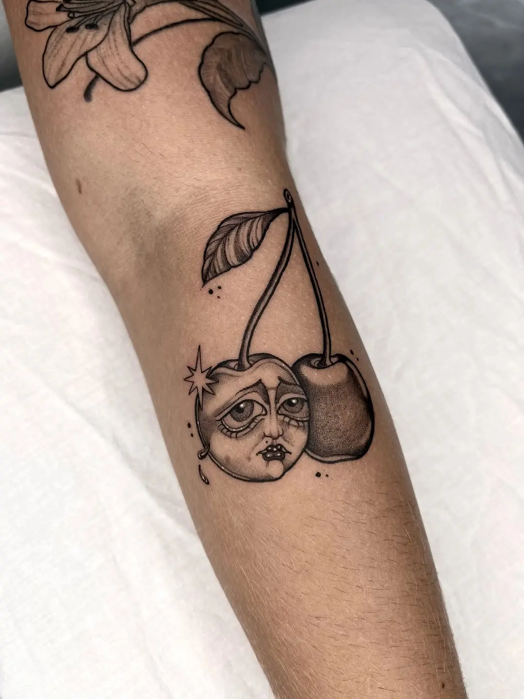 Whimsical cherry tattoo with a moon face