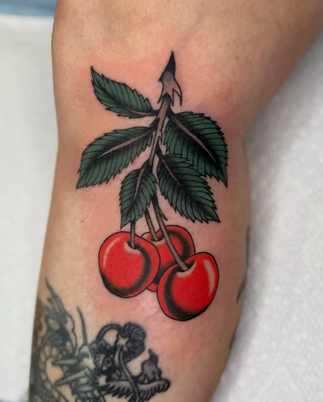 Vibrant cherry tattoo with lush green leaves