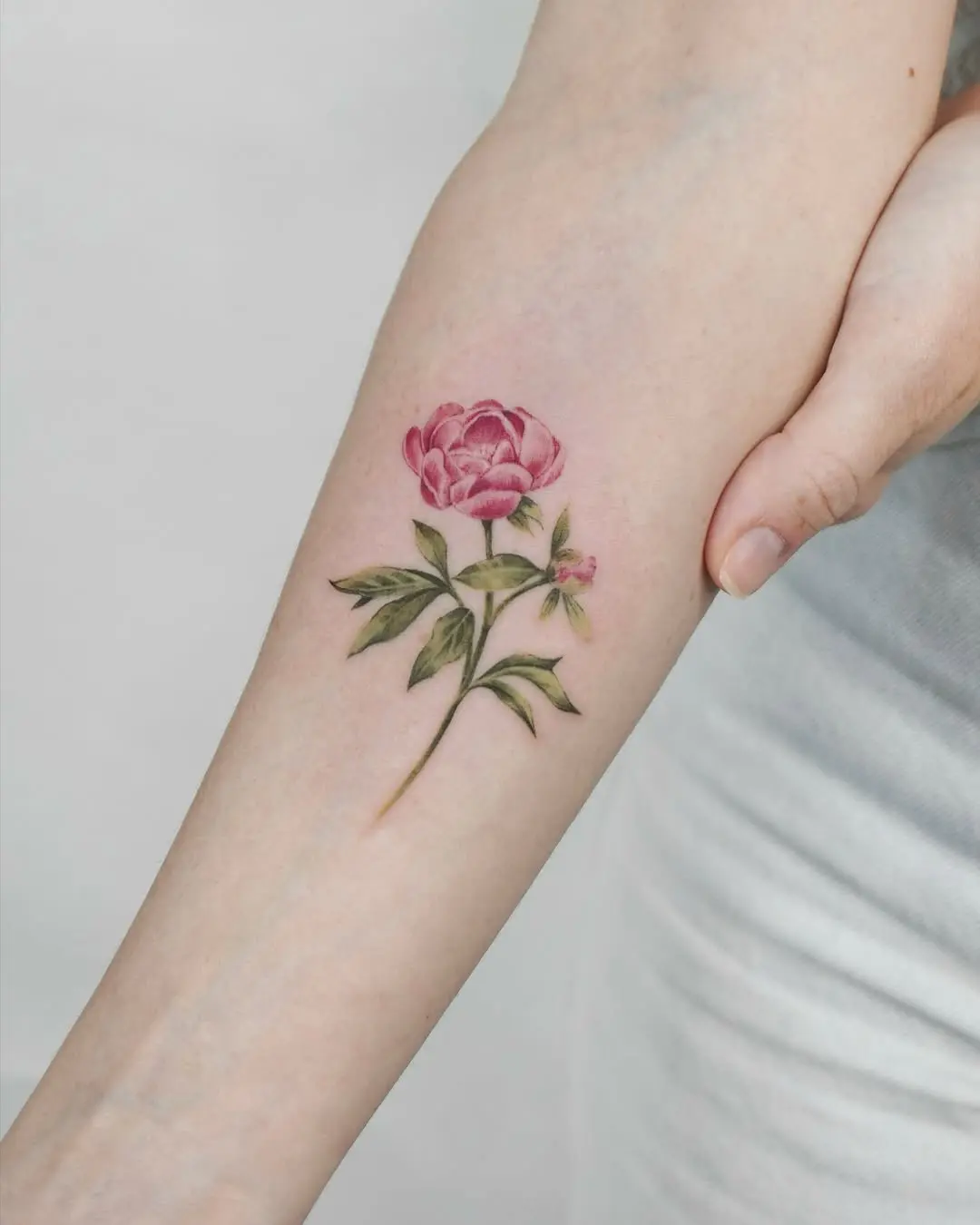 Vibrant peony tattoo on a delicate arm