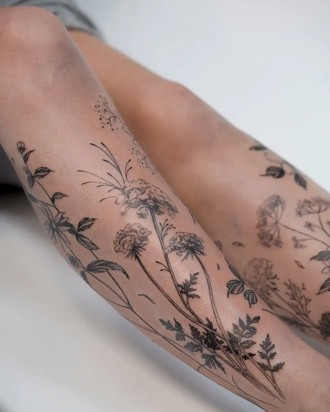 Elegant wildflower tattoos grace the legs.