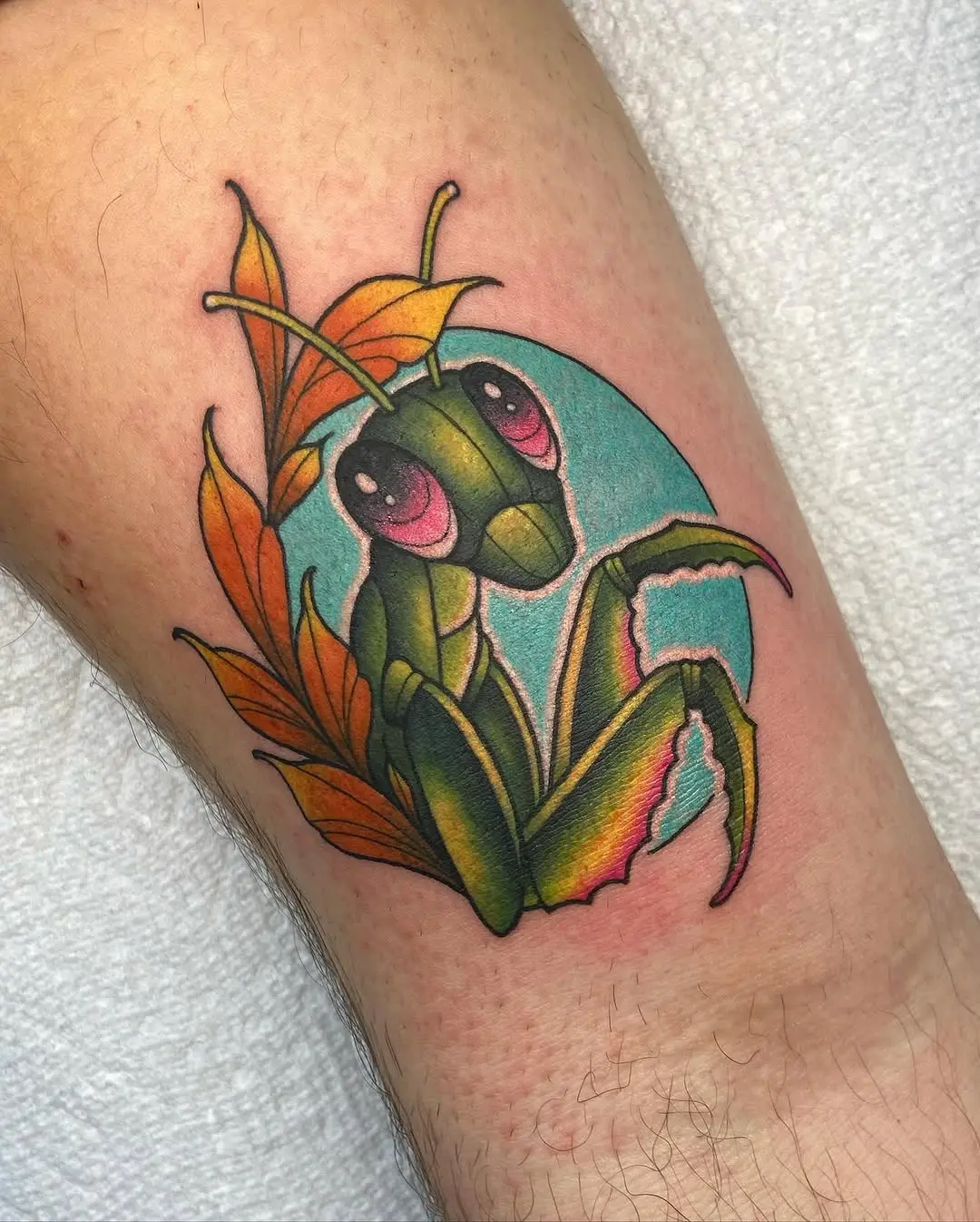 Colorful praying mantis tattoo surrounded by leaves
