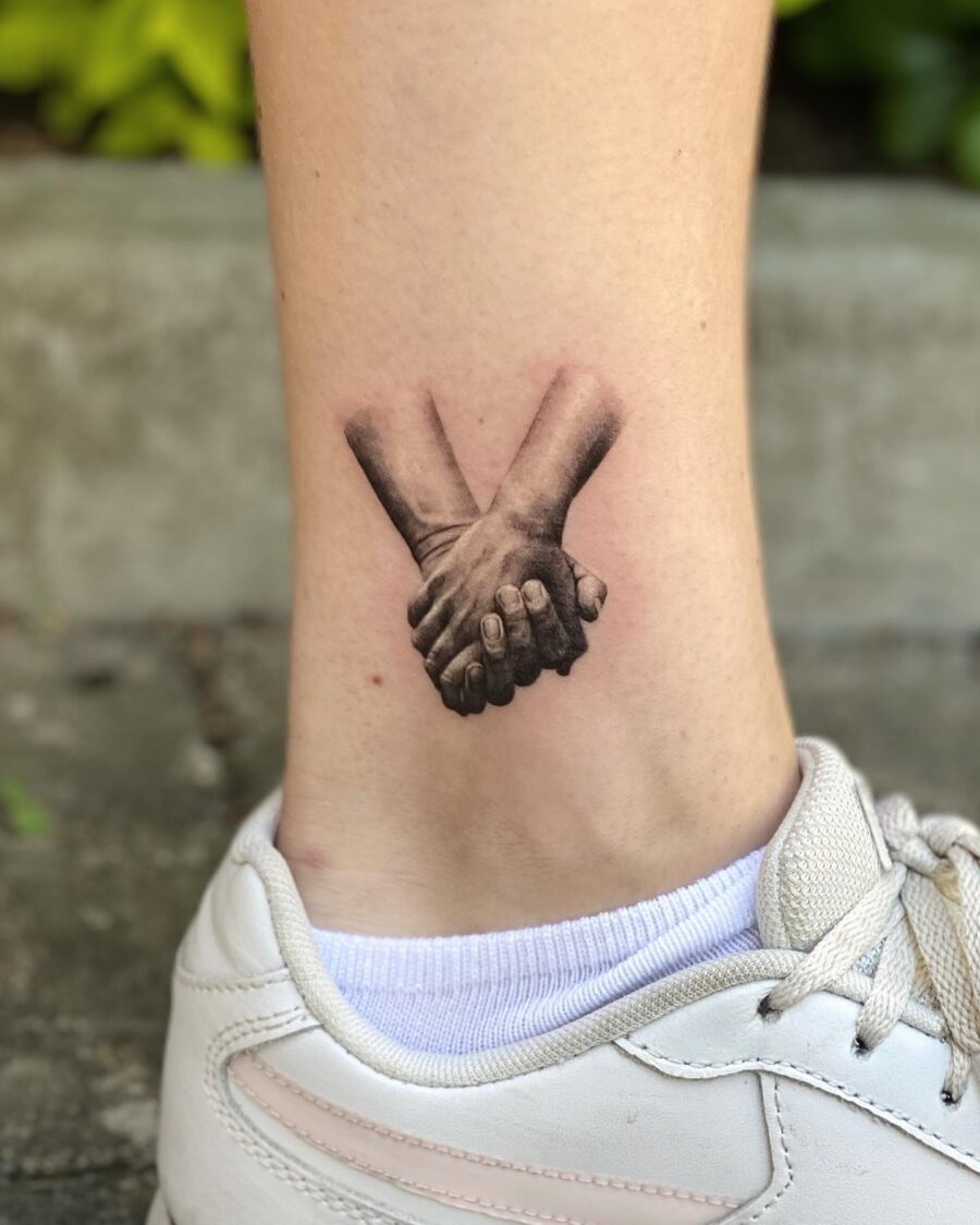 Intricate hand-holding tattoo on the ankle