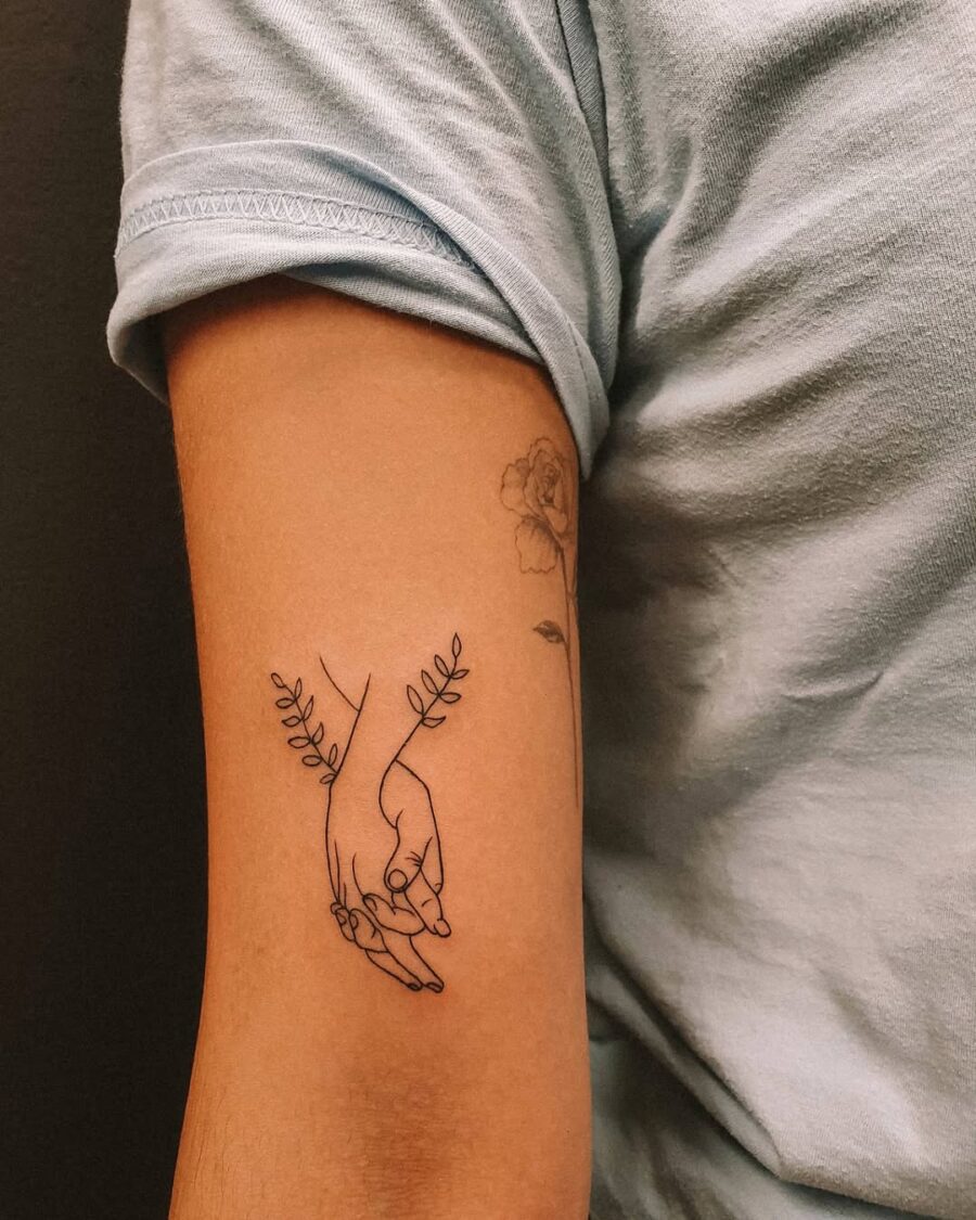 Delicate holding hands tattoo with floral accents
