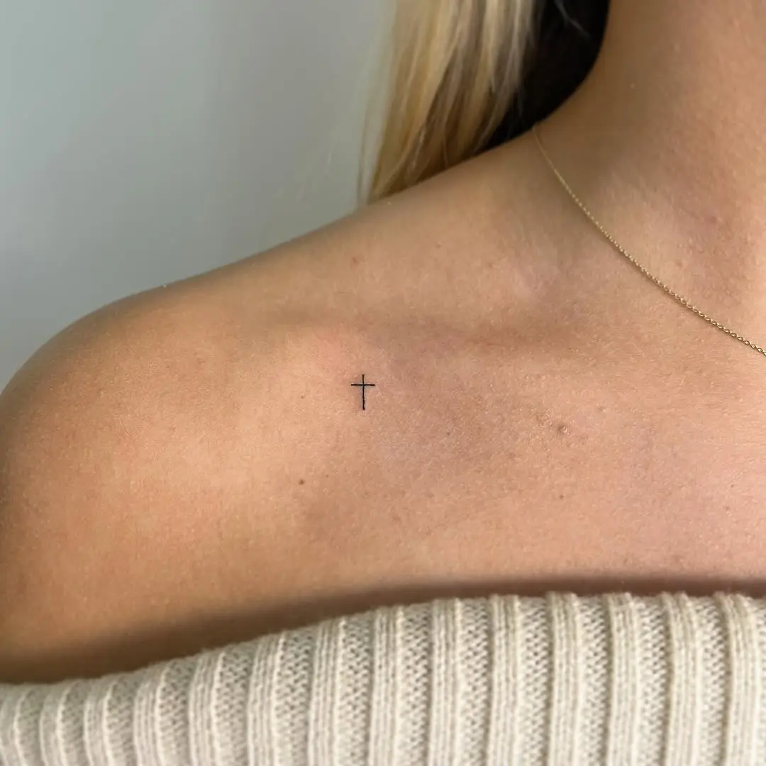 Delicate cross tattoo on the shoulder area
