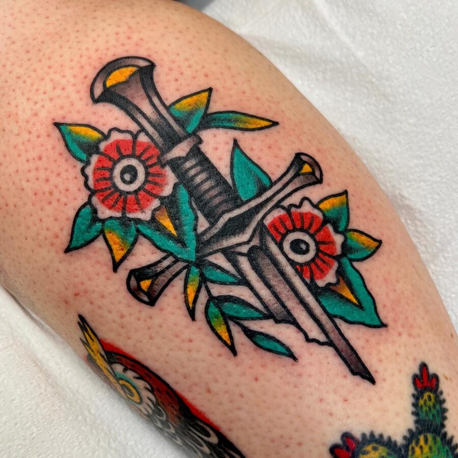 Bold Americana tattoo with dagger and flowers.