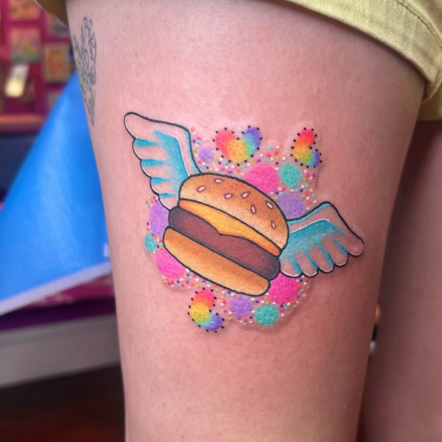 Whimsical burger tattoo with cute wing details