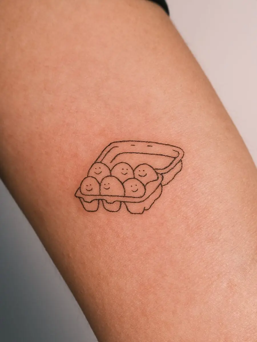 Adorable smiling eggs in a carton tattoo