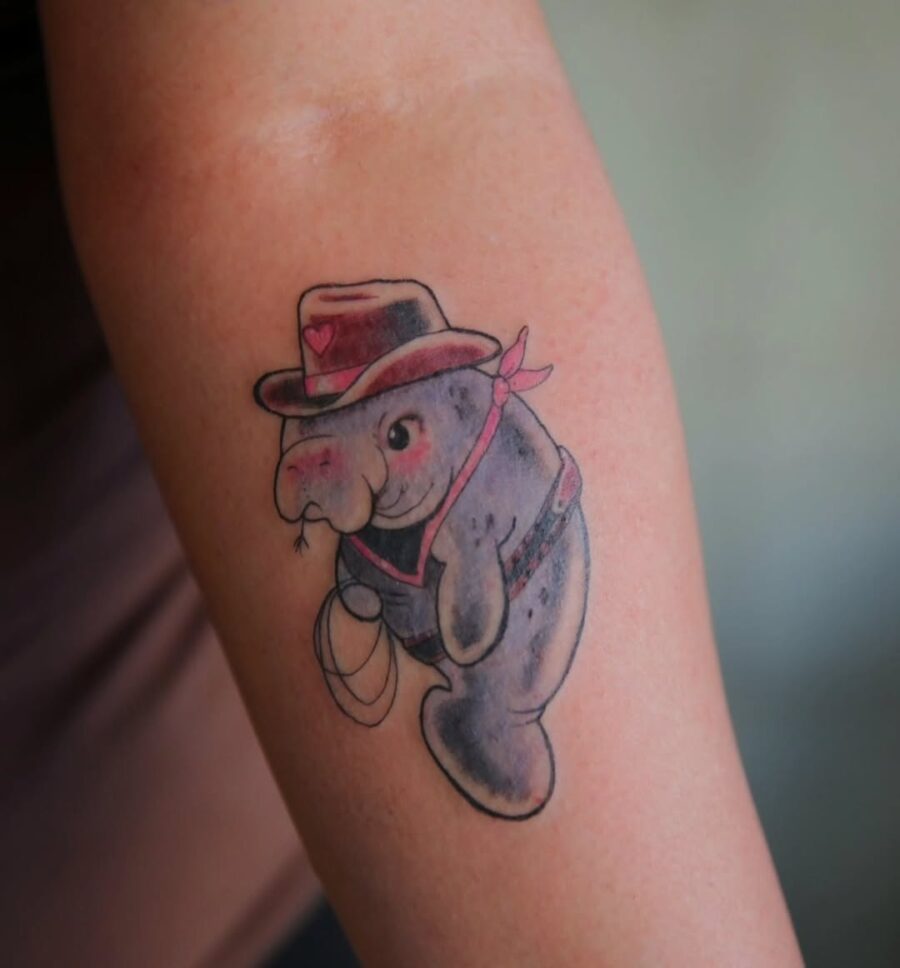 Playful manatee tattoo with cowboy vibes