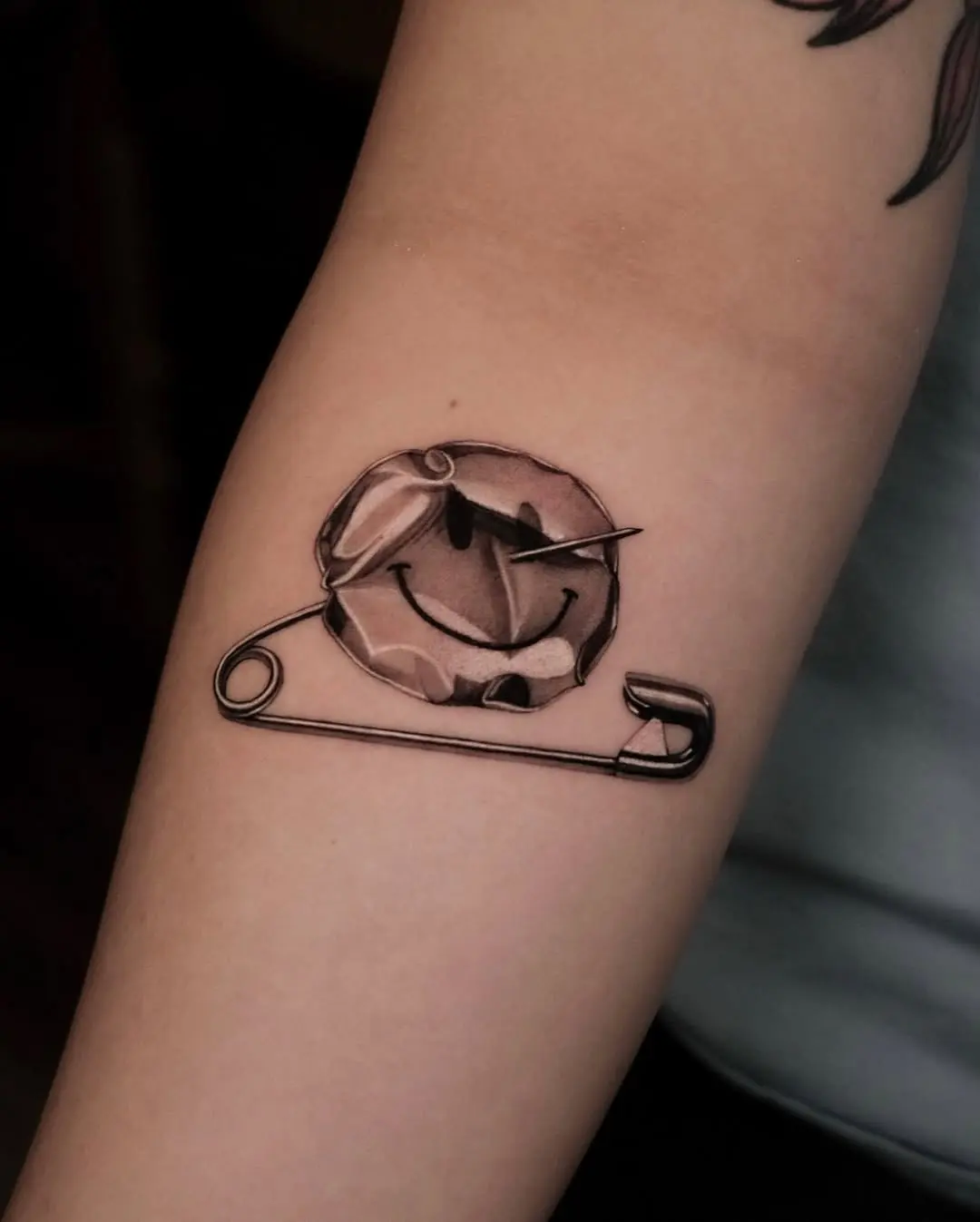 Quirky smiley face tattoo with safety pin