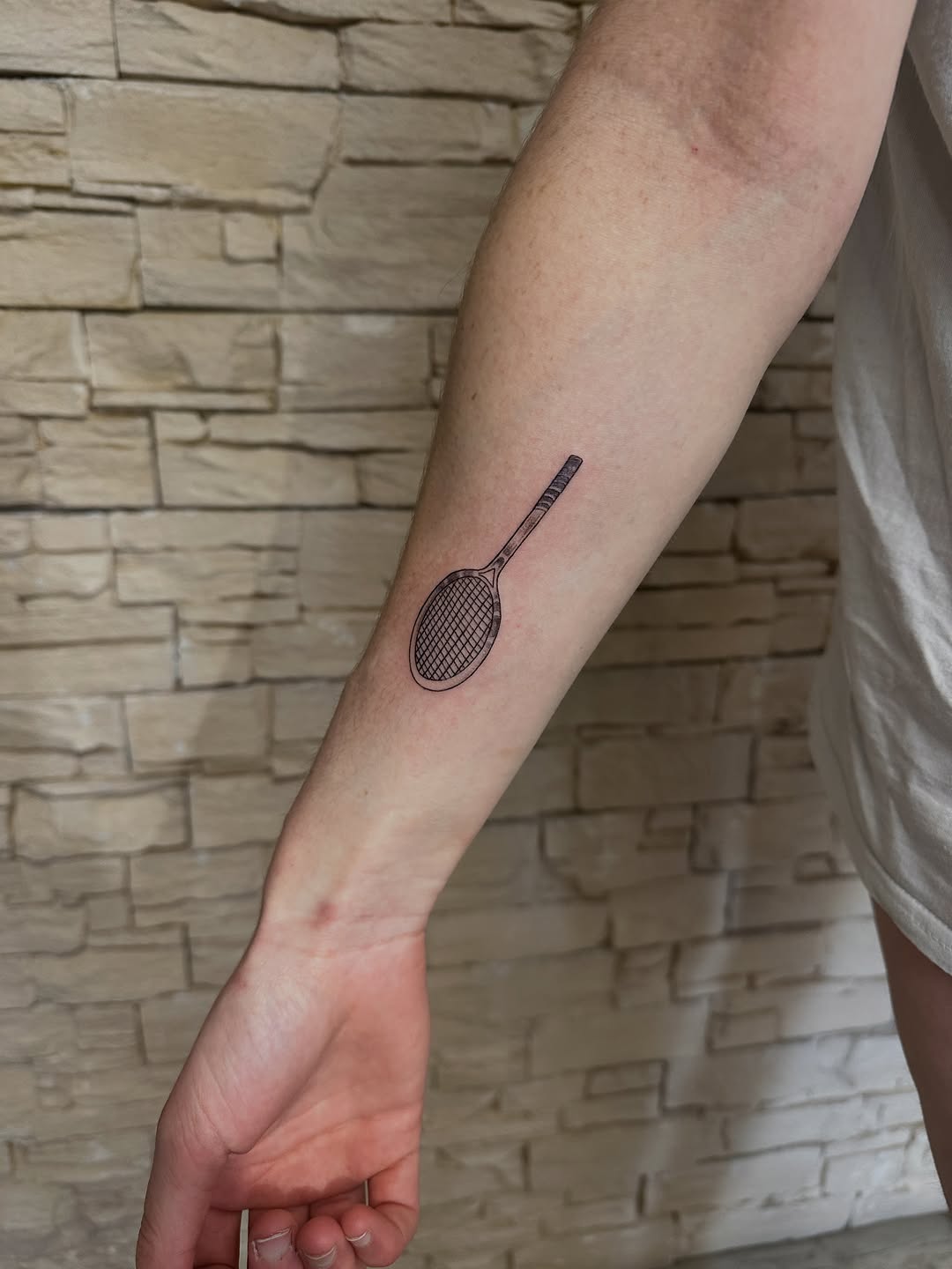 Minimalist tennis racket tattoo on forearm