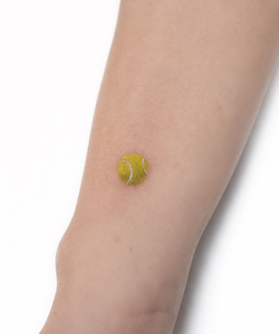 Minimalist tennis ball tattoo on the arm
