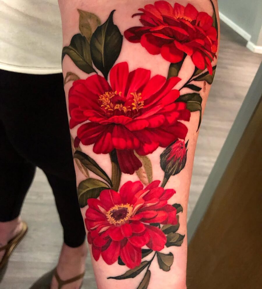 Bold red zinnia tattoo with lush green leaves