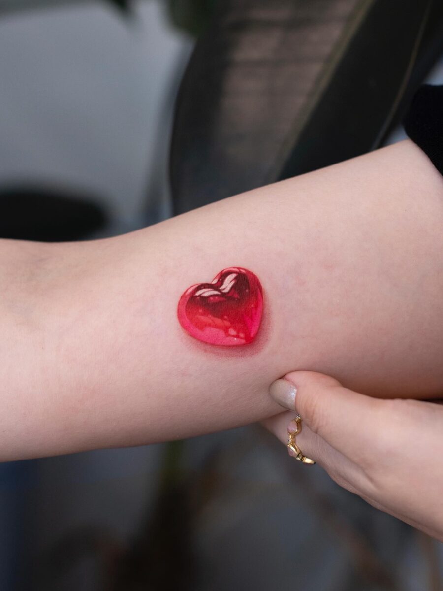 Glossy red heart tattoo on the arm