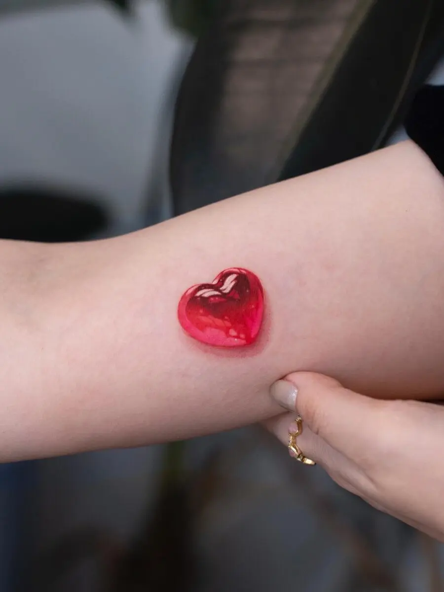 Glossy red heart tattoo on the arm