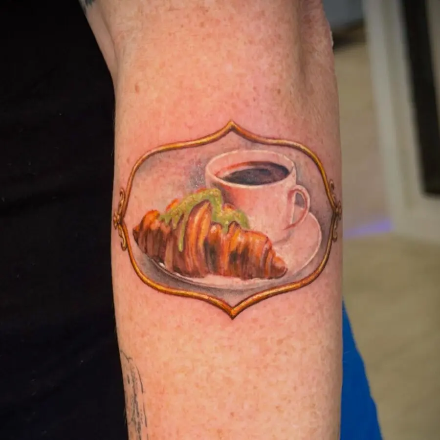 Artistic croissant tattoo featuring coffee cup