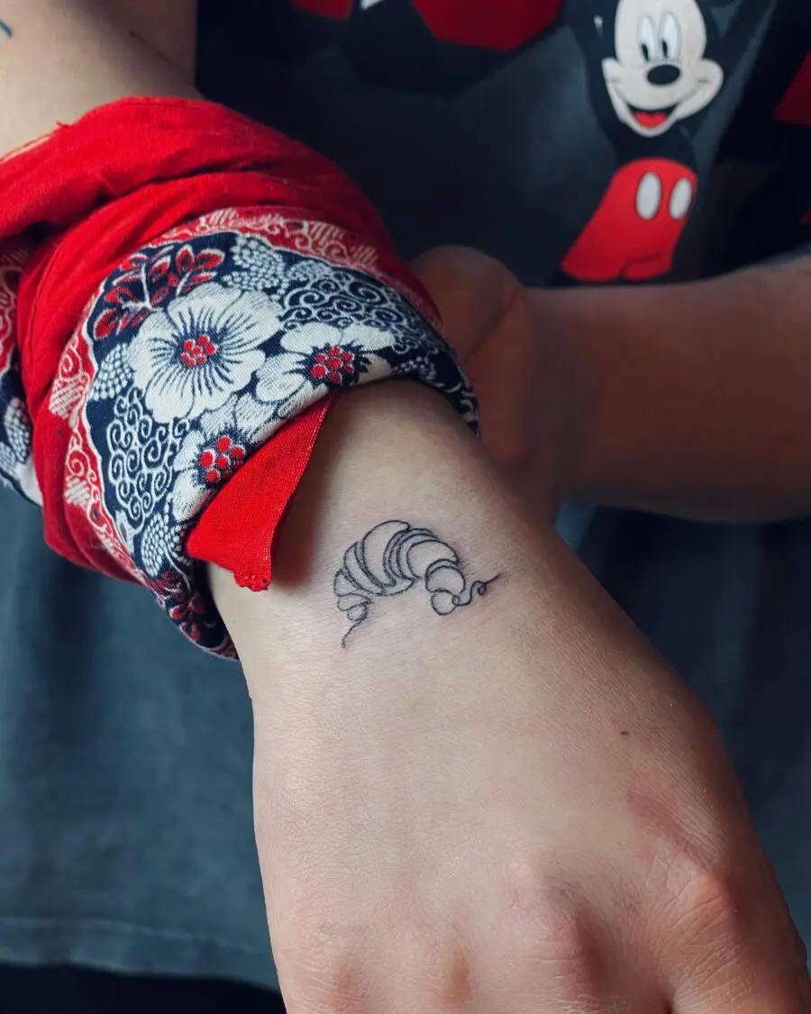 Delicate croissant tattoo on wrist showcases food love