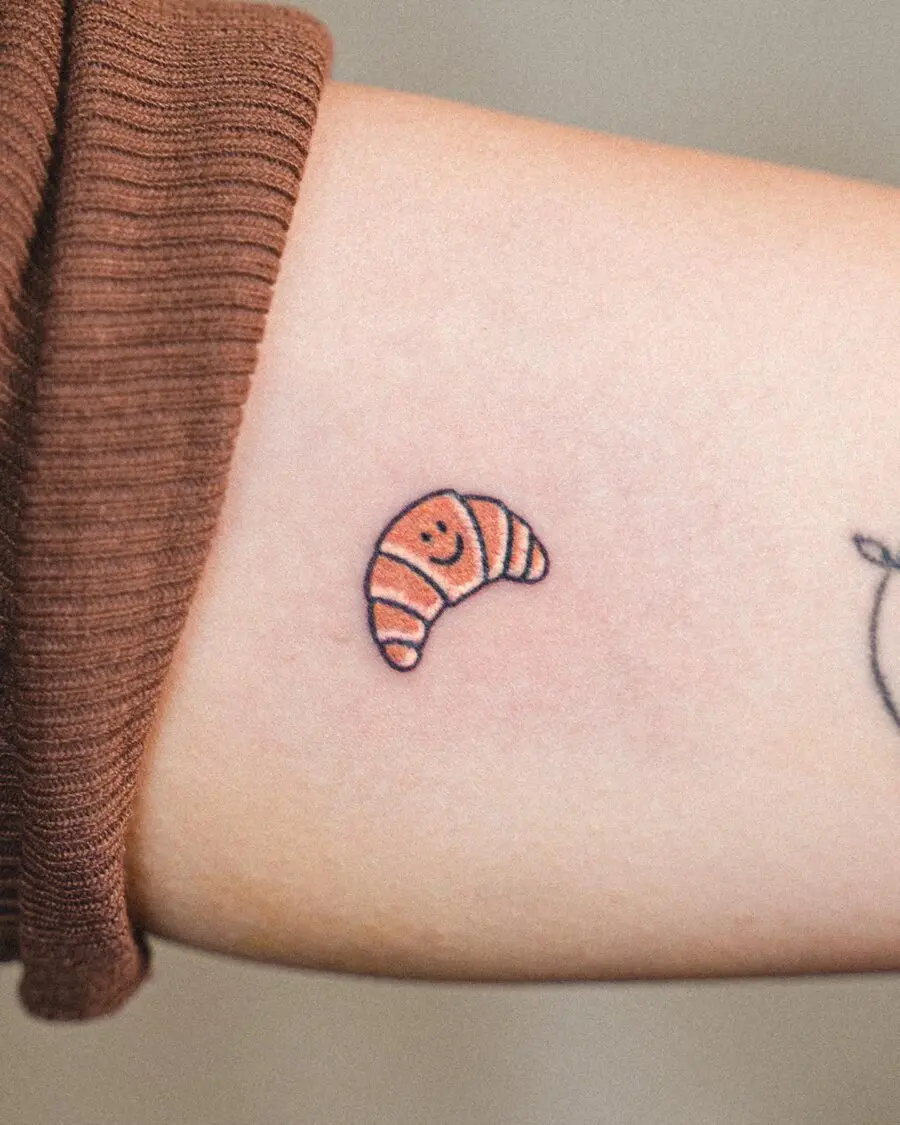 Charming small croissant tattoo with a smile
