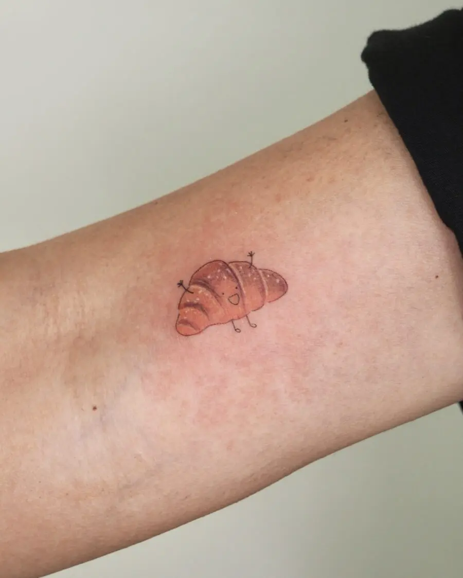 A whimsical croissant tattoo on the forearm
