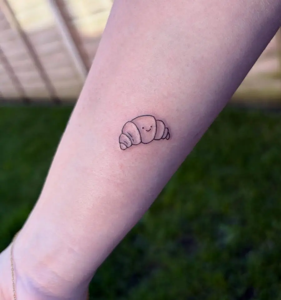 Charming croissant tattoo with a whimsical face
