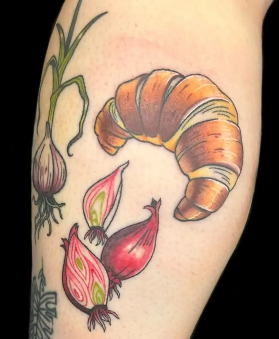 Whimsical croissant tattoo with playful veggies