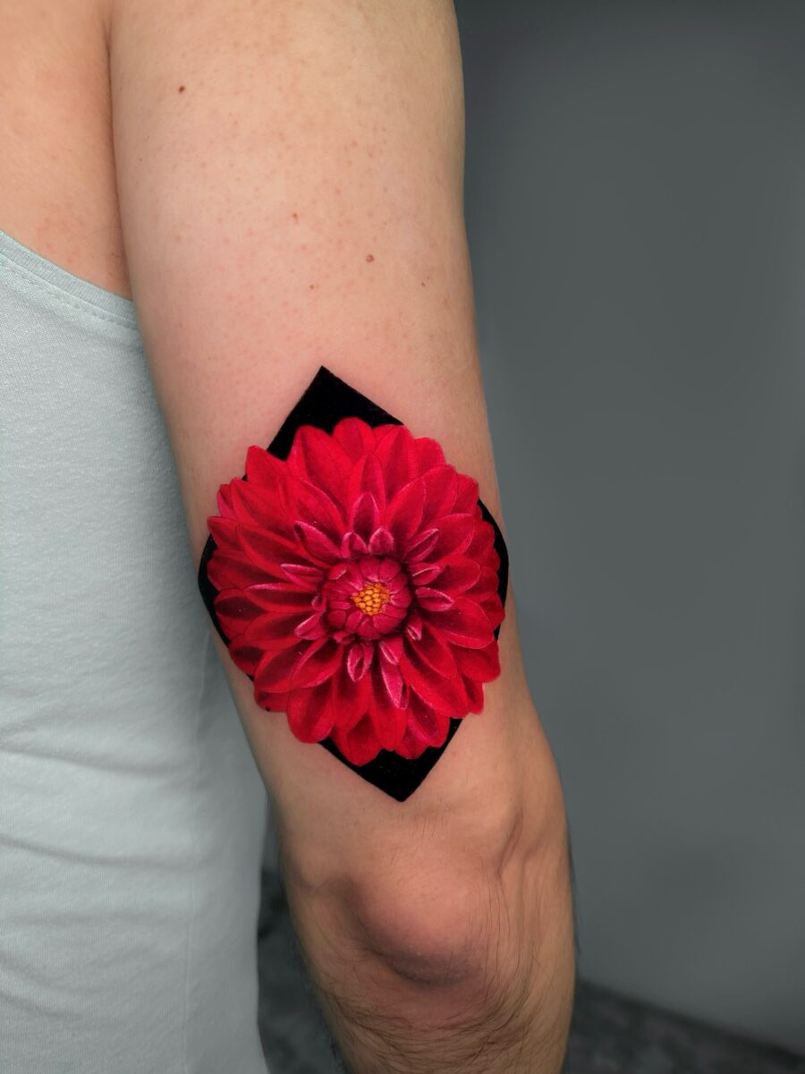Vibrant red dahlia tattoo on the arm