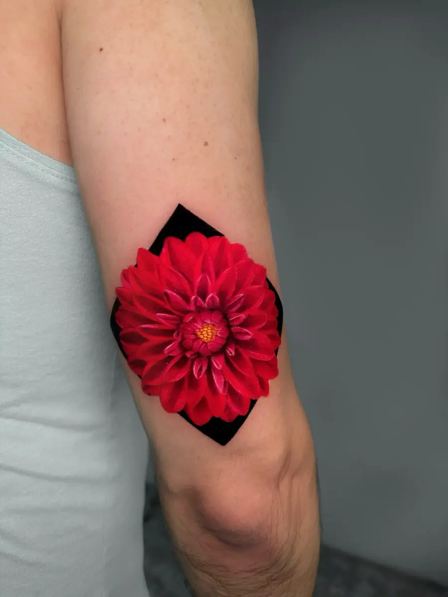 Vibrant red dahlia tattoo on the arm