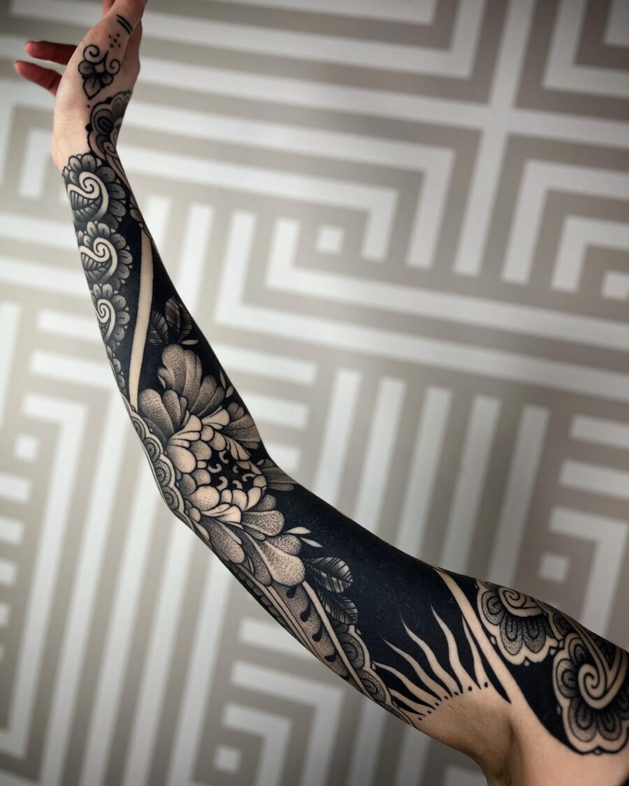 Intricate floral and sun-themed black sleeve tattoo