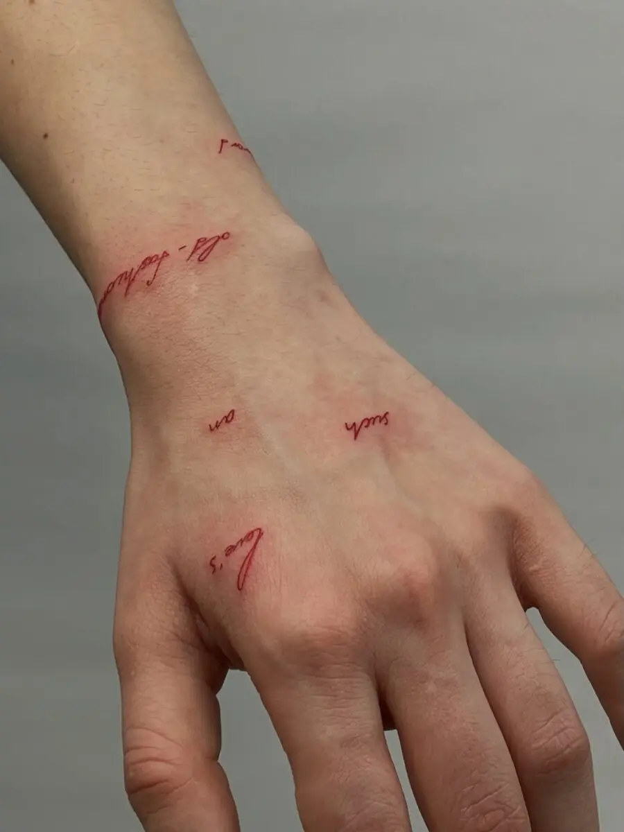 Elegant red script tattoos on the hand