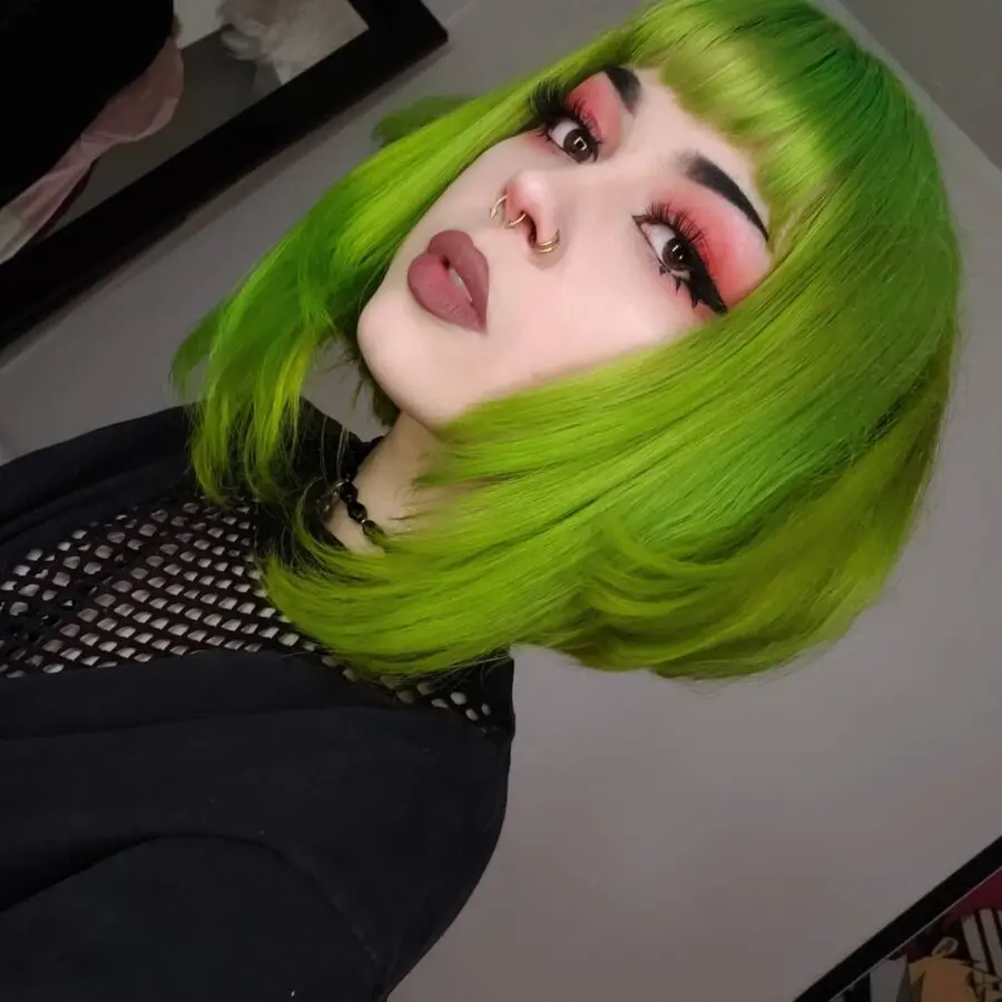 Vibrant green hair with dramatic eye makeup.