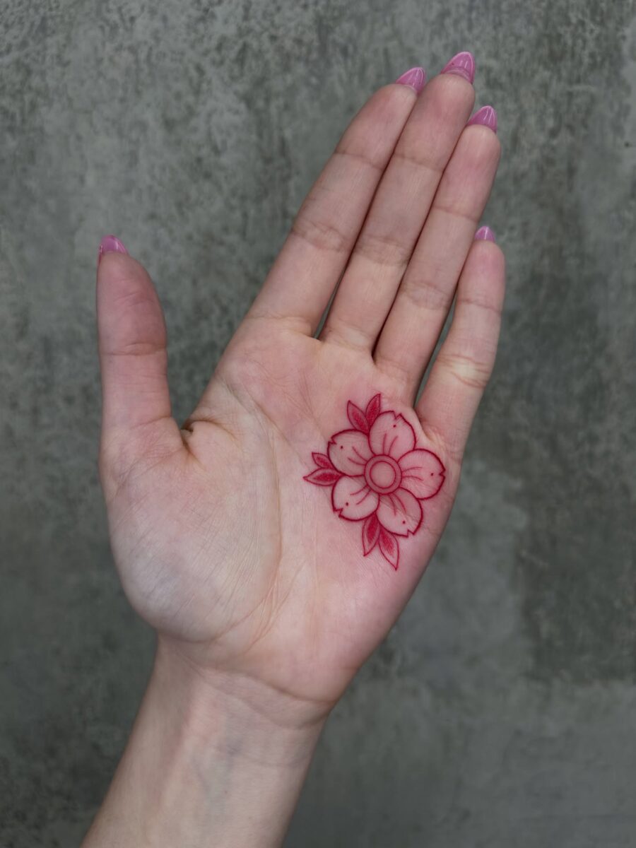 Delicate red ink flower tattoo on palm