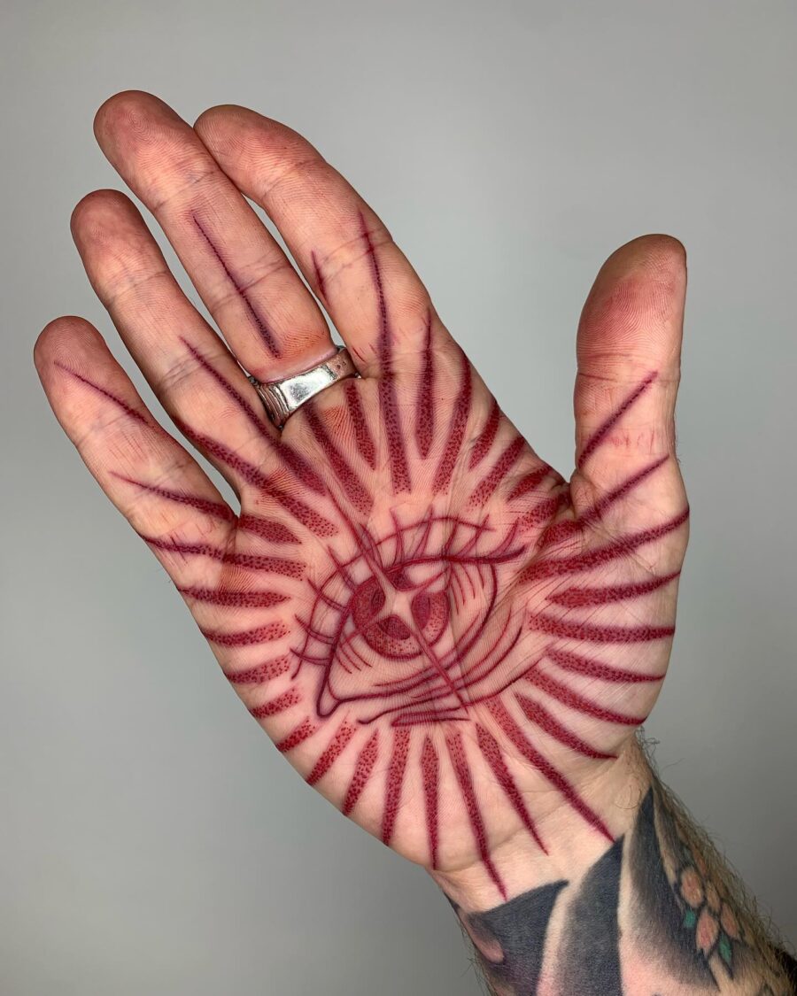 Intricate red ink eye tattoo design in hand