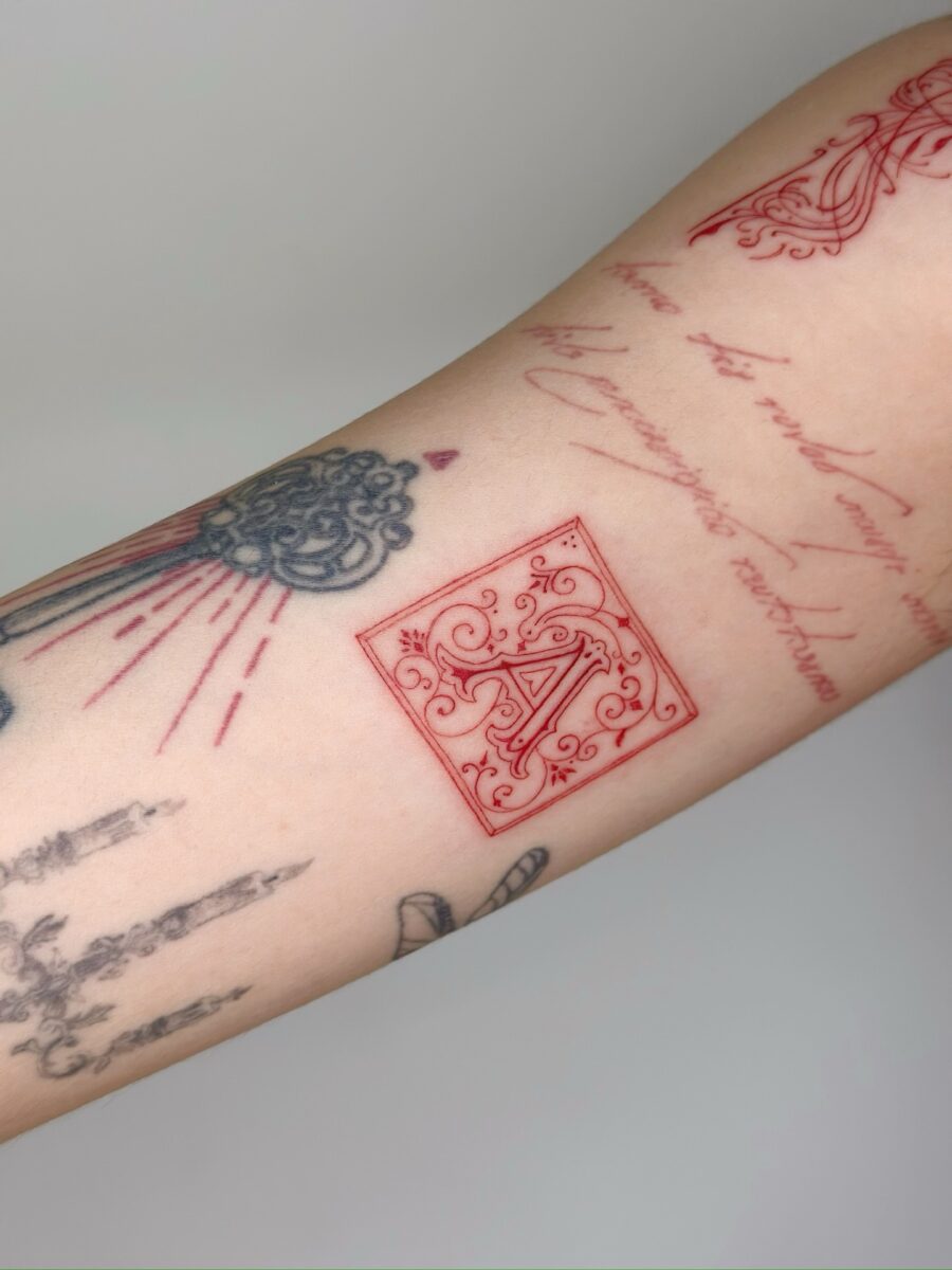 Elegant red ink initials on tattooed arm
