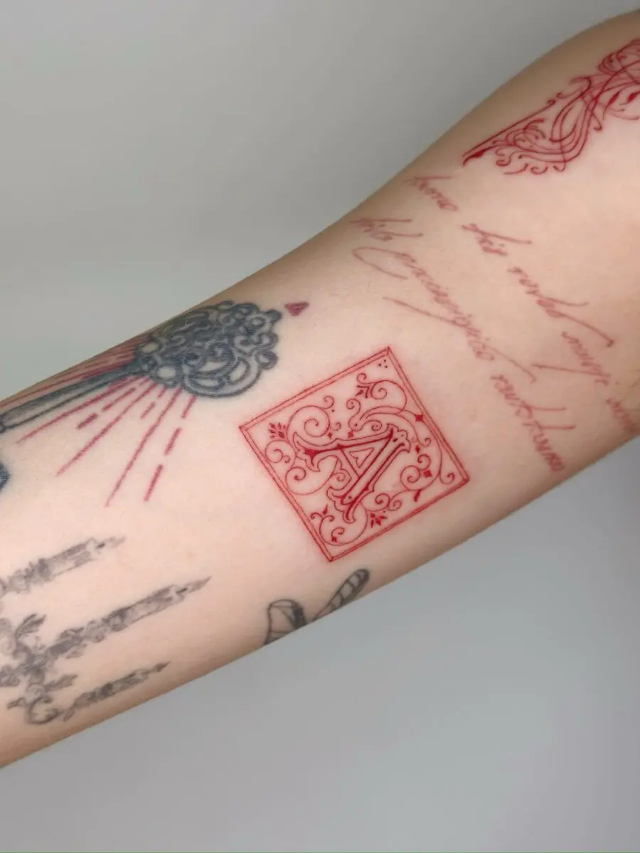 Elegant red ink initials on tattooed arm