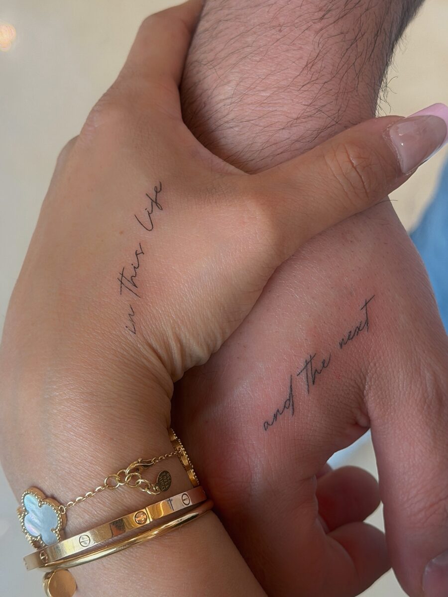 Delicate script tattoos on intertwined hands