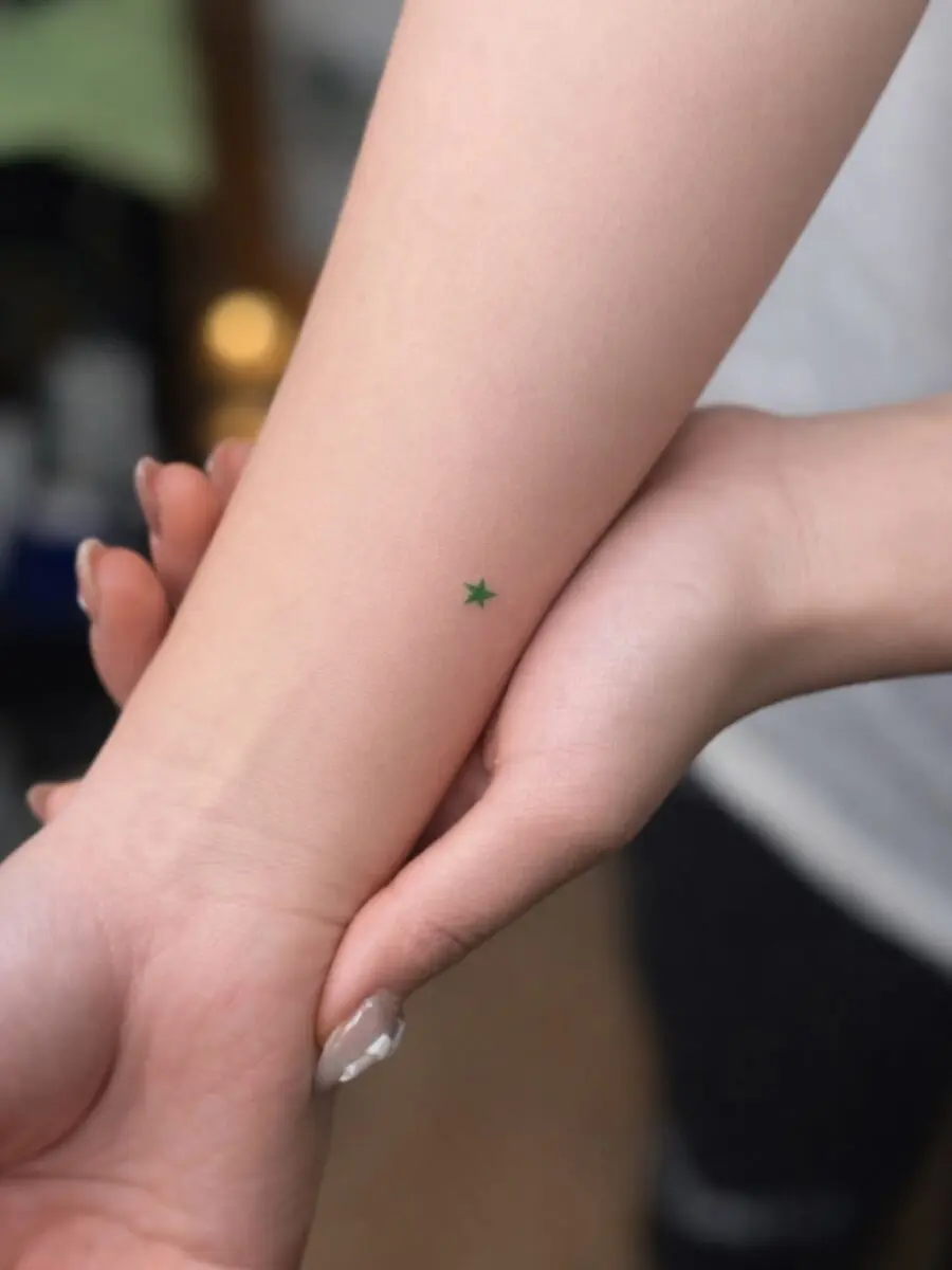 Minimalist green star tattoo on the arm